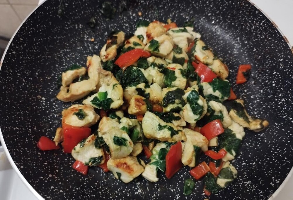 Mixture of chicken breasts, spinach and paprika in a frying pan with butter