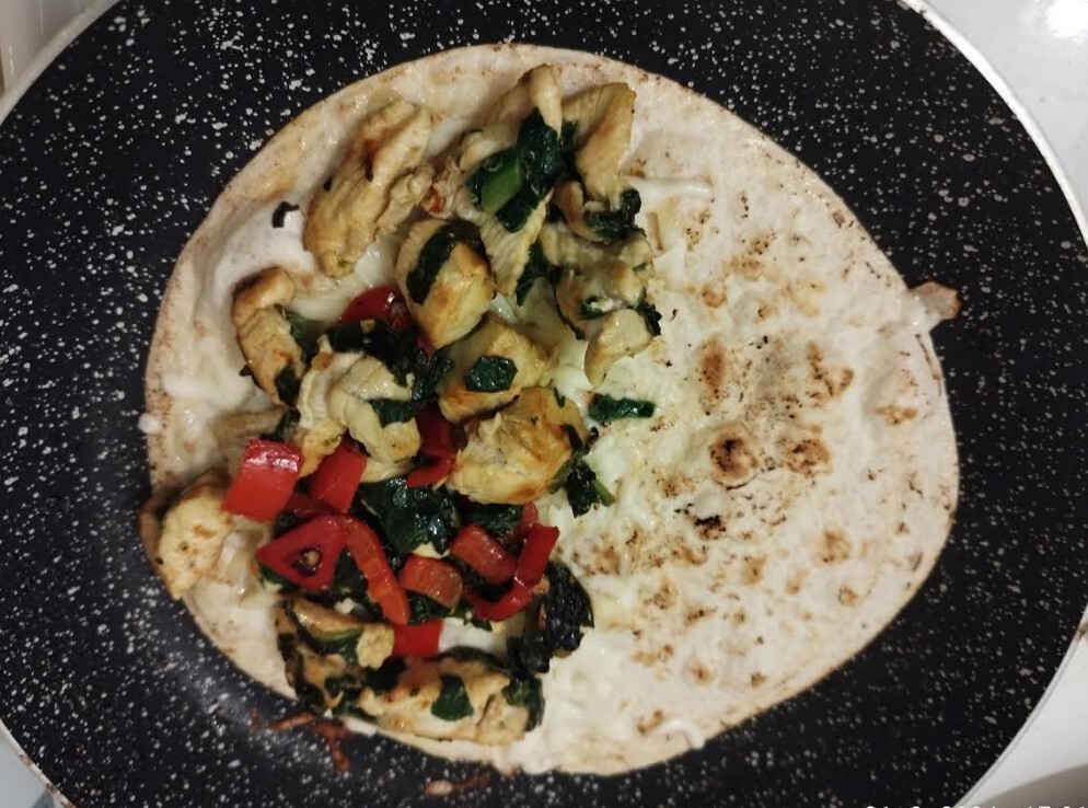 Mixture of chicken breats, spinach and paprika on top of cheese on a tortilla in a frying pan