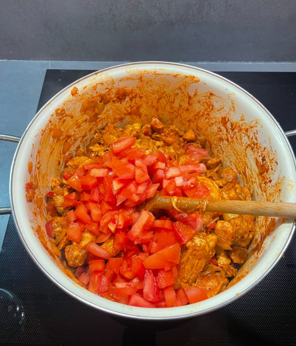 adding chopped tomato to chicken goulash